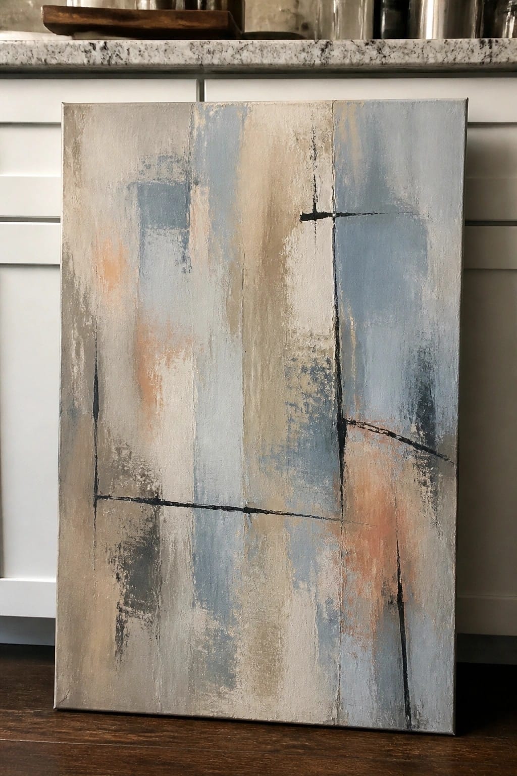 Abstract canvas with blue gray beige tones and black lines leaning against kitchen cabinets