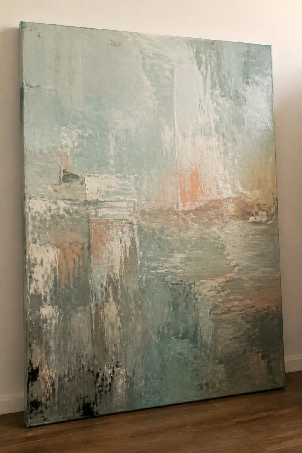 Large abstract painting with textured teal, orange, and white strokes leaning on floor