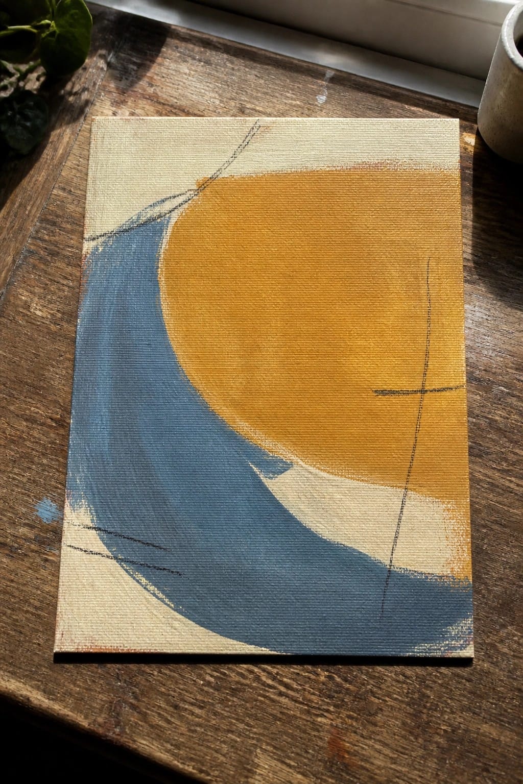 Abstract painting with blue curve and orange circle on wooden table beside plant