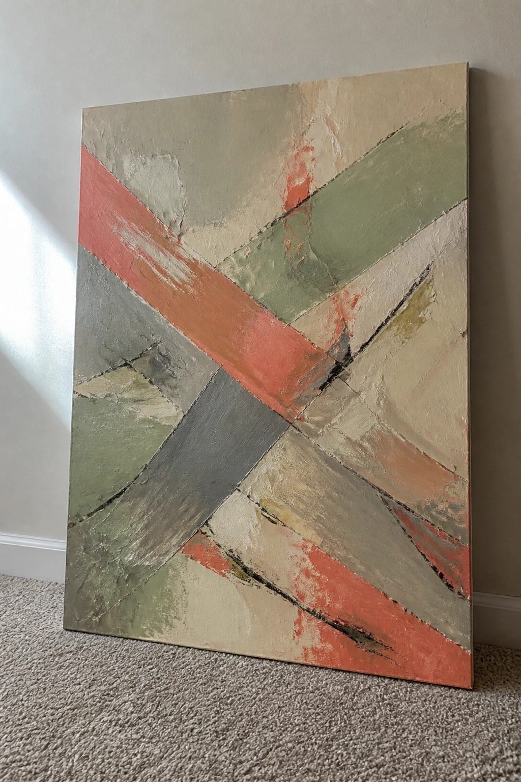 A large abstract oil painting leaning against a wall, featuring intersecting diagonal bands in coral red, sage green, gray, and beige with visible brushstrokes and texture.