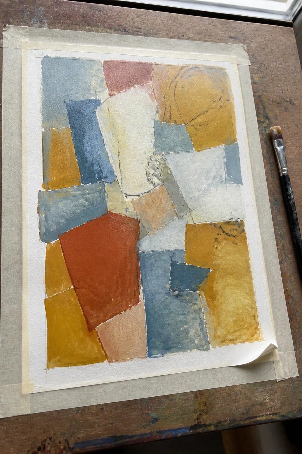 Abstract painting of overlapping colored rectangles on paper beside a paintbrush.
