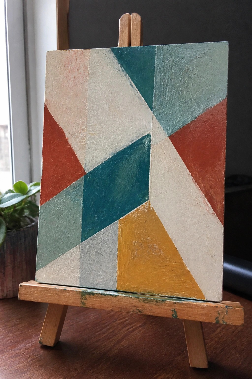Abstract geometric painting with red, teal, beige, and yellow shapes on wooden easel