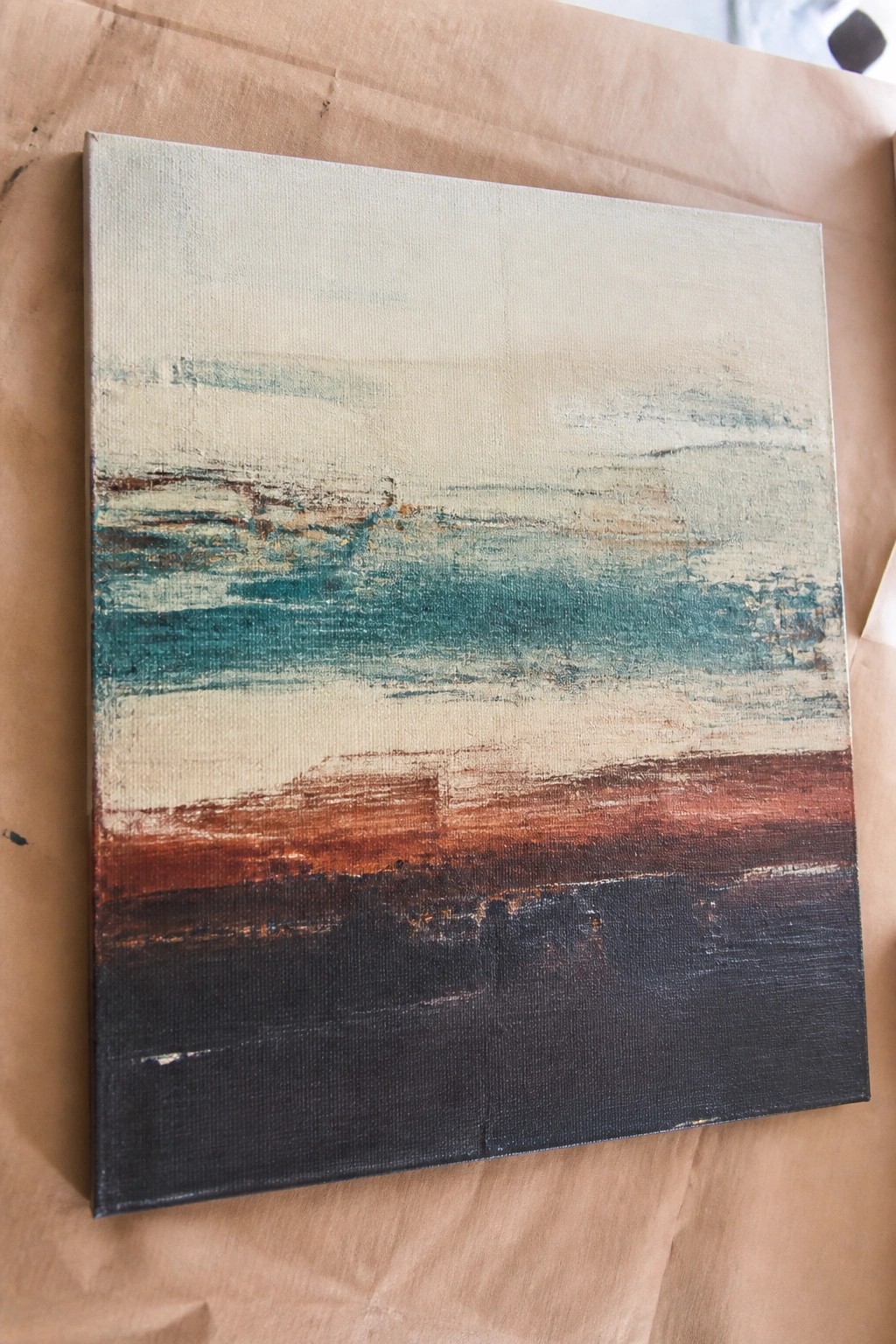 Abstract canvas with horizontal teal, brown, and black brushstrokes on brown paper.
