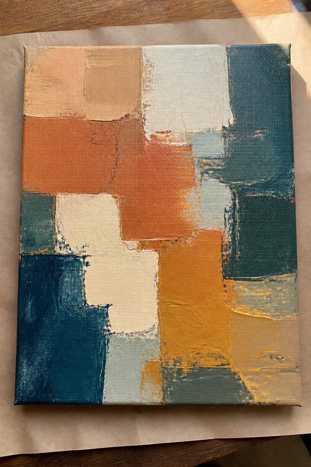 Abstract acrylic painting with overlapping geometric blocks in orange, teal, white, and yellow.