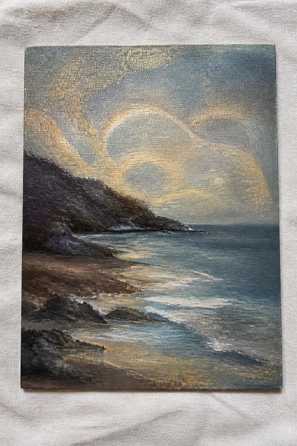 Painting of waves on a sandy beach with dark cliffs and golden swirling clouds.