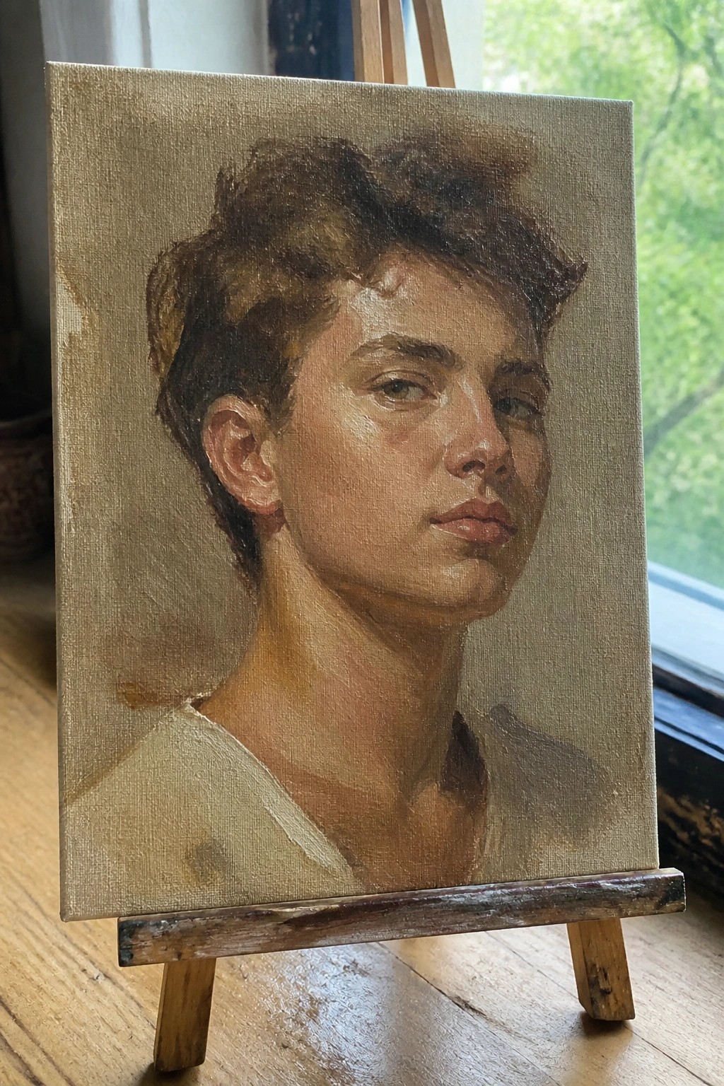 Oil painting of young man with short brown hair on wooden easel by window
