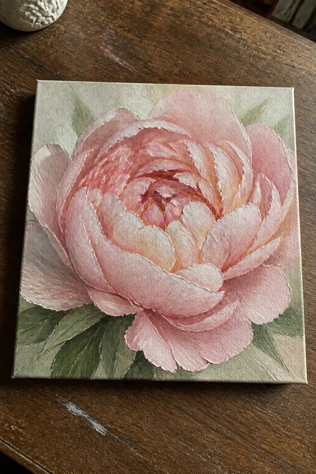 Square canvas with blooming pink peony painting on dark wooden table