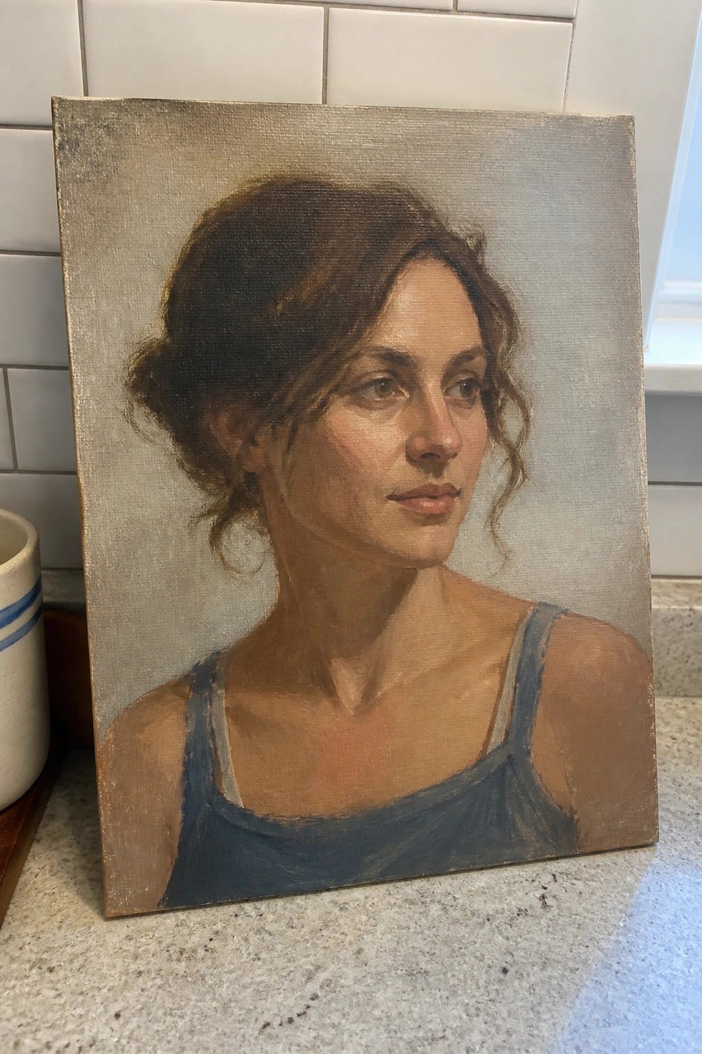 Realistic oil painting of a woman with brown hair in a bun, wearing a blue tank top, looking slightly to her right against a plain gray background.