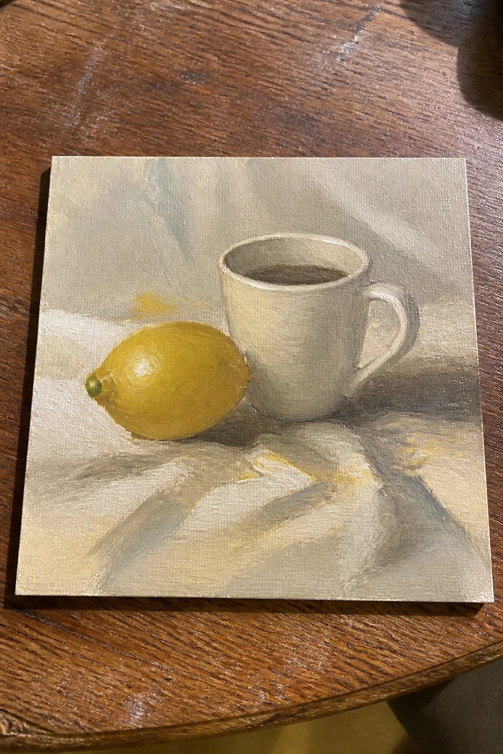 Realistic oil painting of yellow lemon beside white mug on draped cloth with shadows