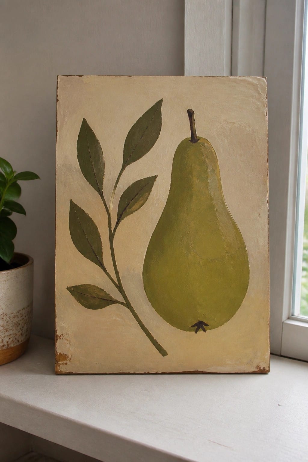 Green pear with stem and leaves painted on textured beige canvas on windowsill