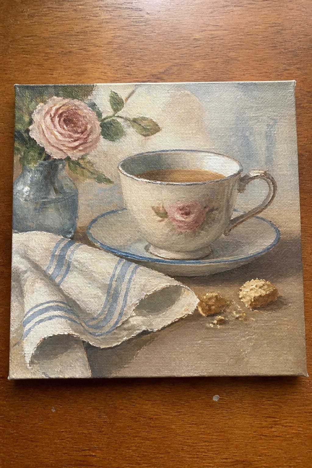 Still life with rose-patterned teacup, pink rose in vase, striped cloth, and cookies.