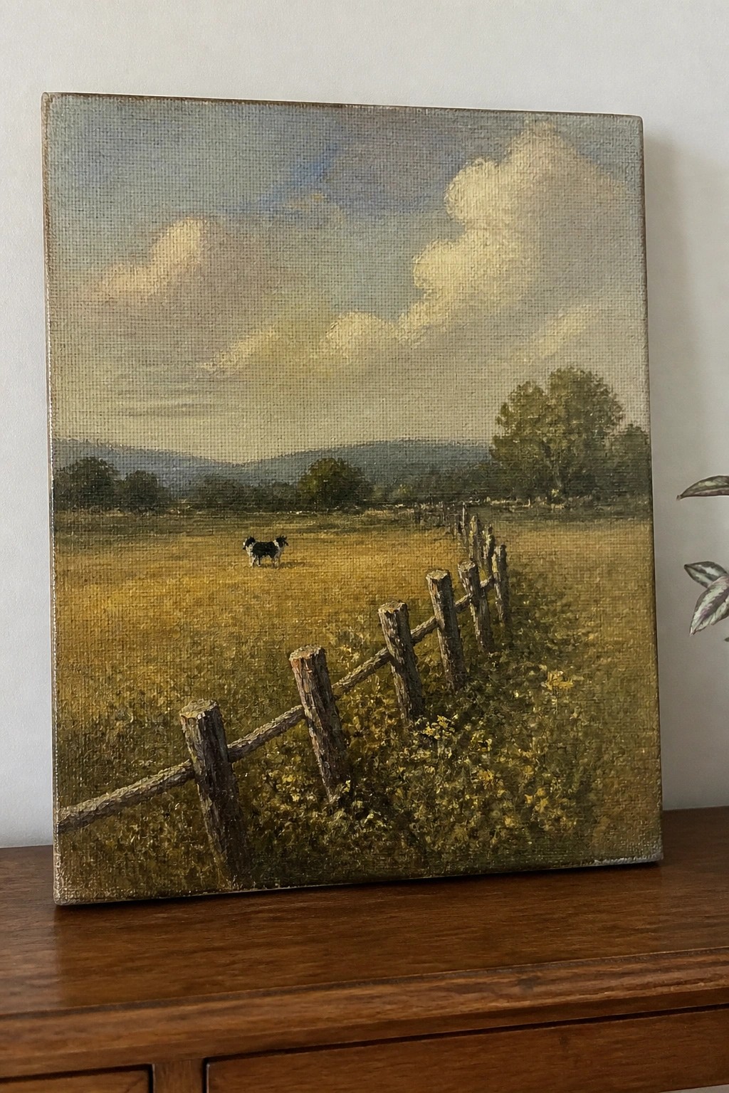 Landscape painting shows dog standing in field beside wooden fence under cloudy sky