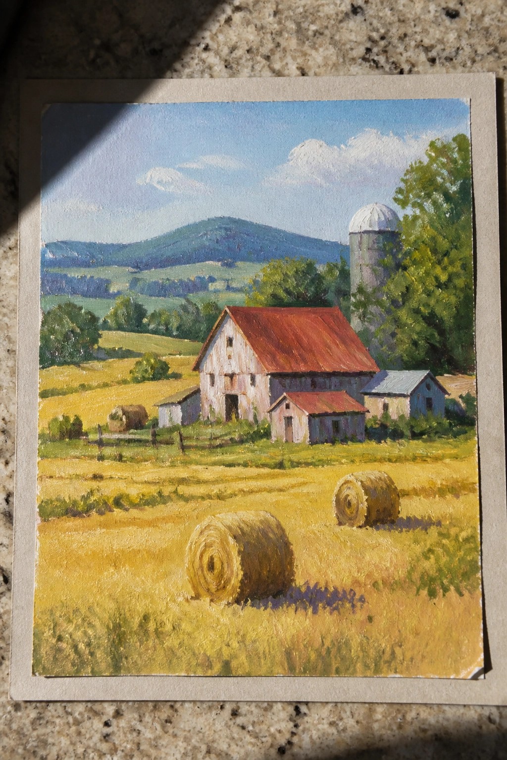 Realistic painting of weathered barn with red roof, silo, and hay bales in fields.