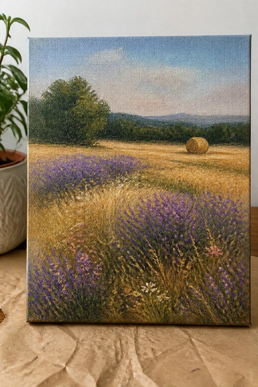 Landscape painting of purple wildflowers in golden field with hay bale and blue sky.