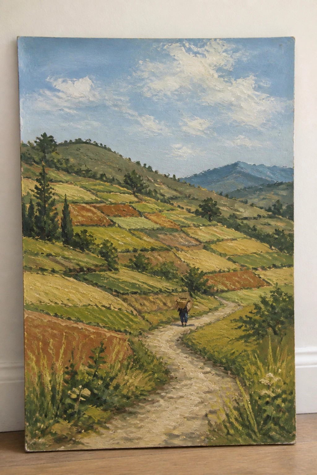 Person in blue carries basket along path through terraced green and brown hills.