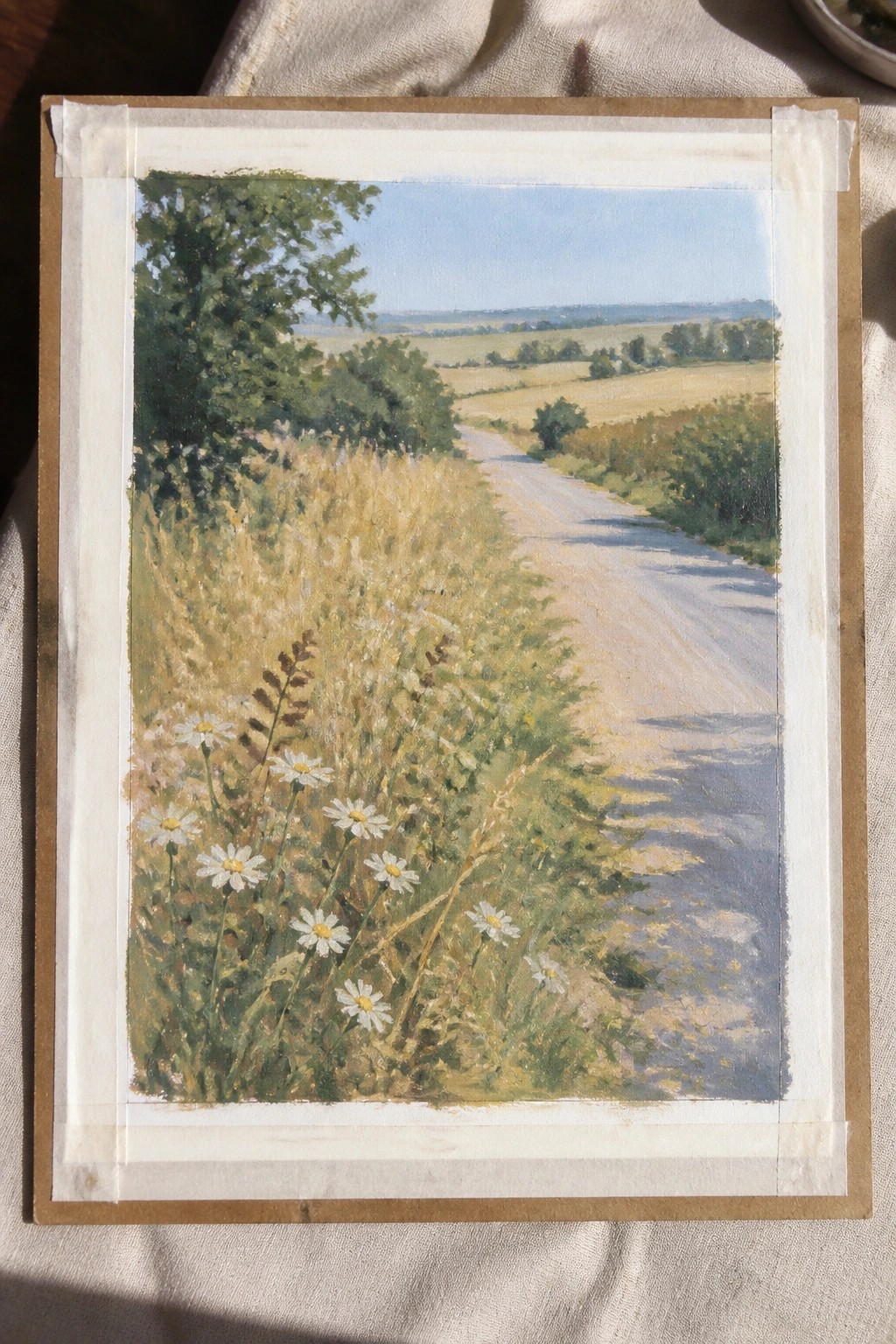 Landscape painting of winding dirt road with white daisies, golden fields, and blue sky