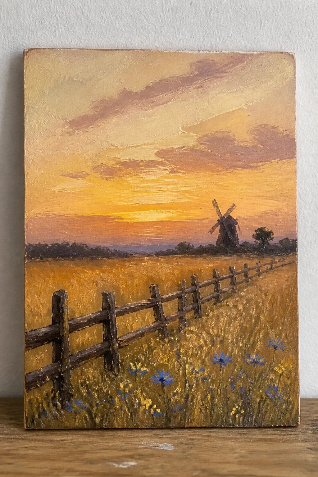 Sunset landscape painting with wooden fence, wildflowers, golden field, and distant windmill.