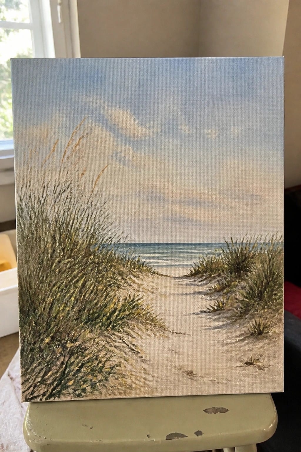 Painting of sandy path through grassy dunes leading to calm ocean under cloudy sky.