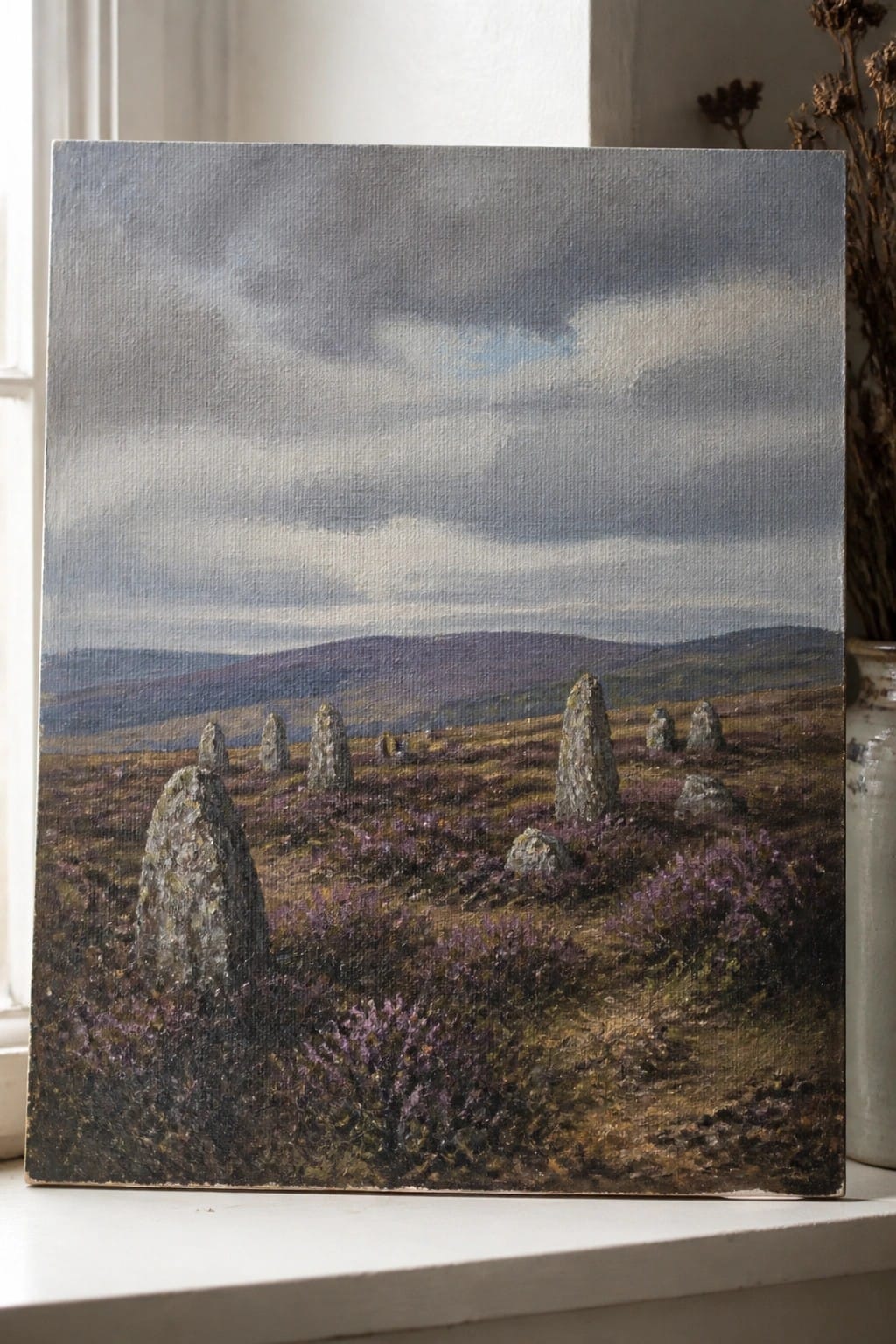 Oil painting of standing stones amid purple heather moorland under cloudy skies on windowsill