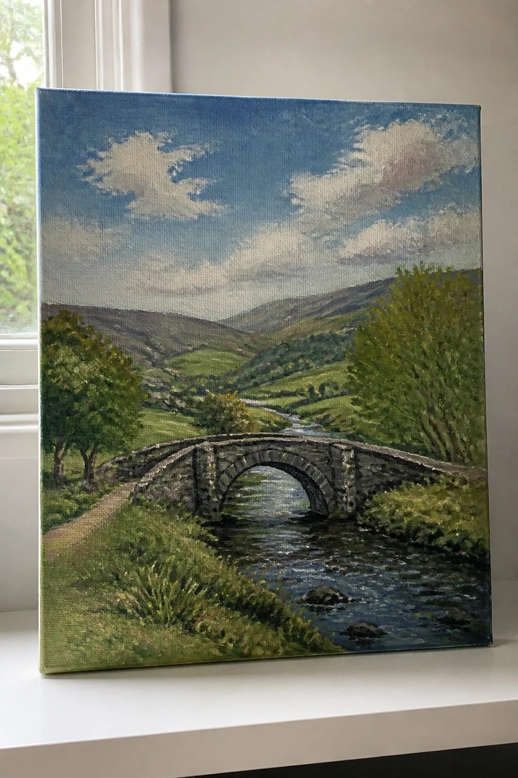 A realistic oil painting of a stone bridge arching over a river in a green valley with hills and trees under a blue sky.