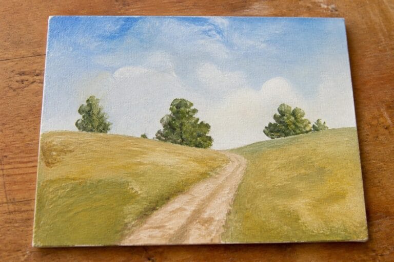 23 Beautiful Easy Landscape Oil Painting Ideas Using Hills, Trees, and Open Skies Winding dirt path through rolling green hills with trees under blue sky on wood