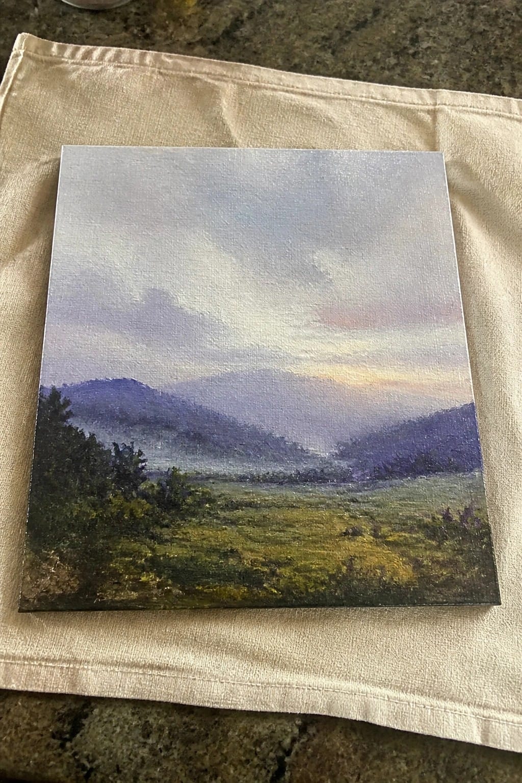 Canvas painting of misty purple mountains over green fields at dawn