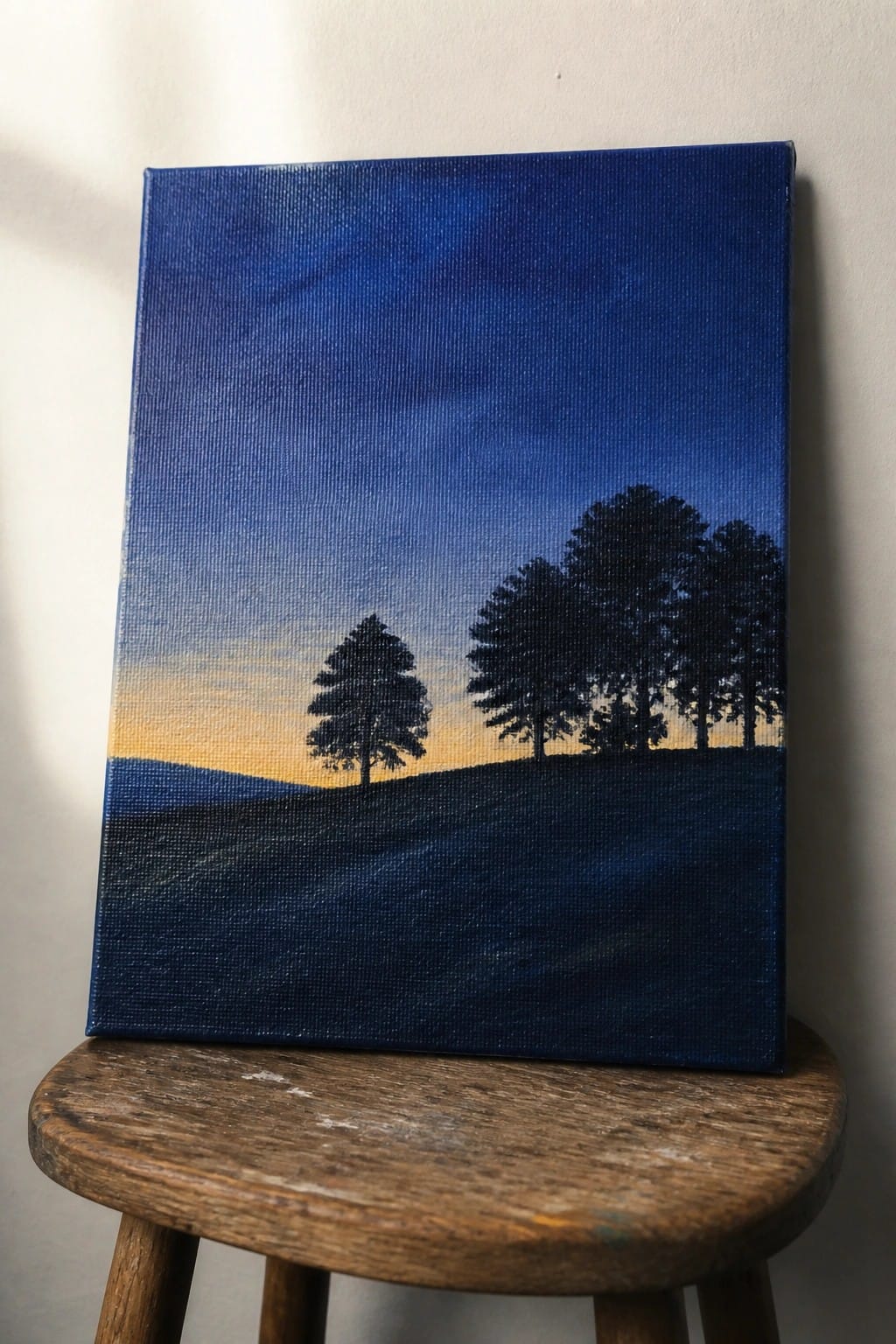 Silhouetted trees on dark hills under blue-orange sunset sky, on wooden stool.