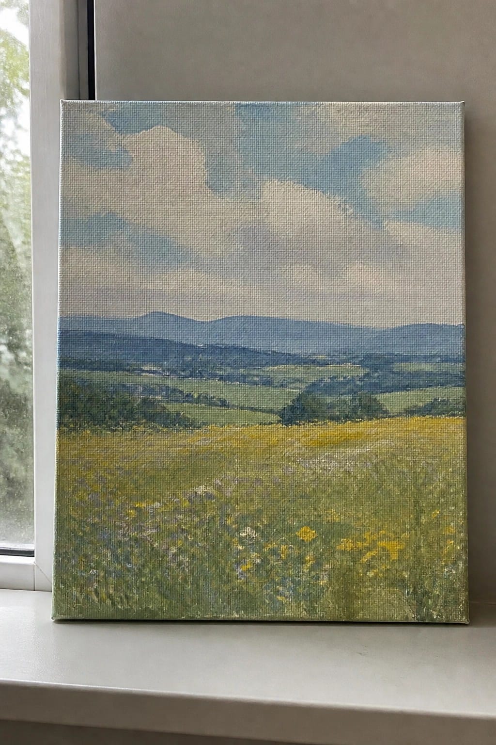 Landscape painting of yellow wildflower meadow with blue hills on windowsill