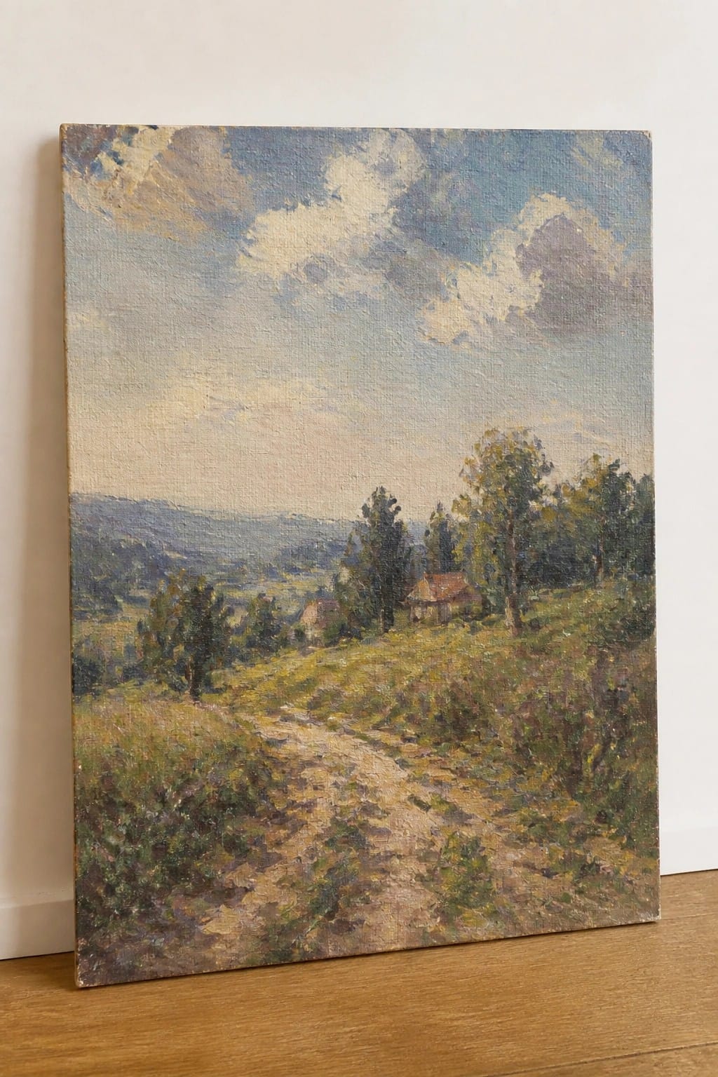 An oil painting of a dirt path winding through grassy fields with trees, small houses, rolling hills, and a large cloudy sky.