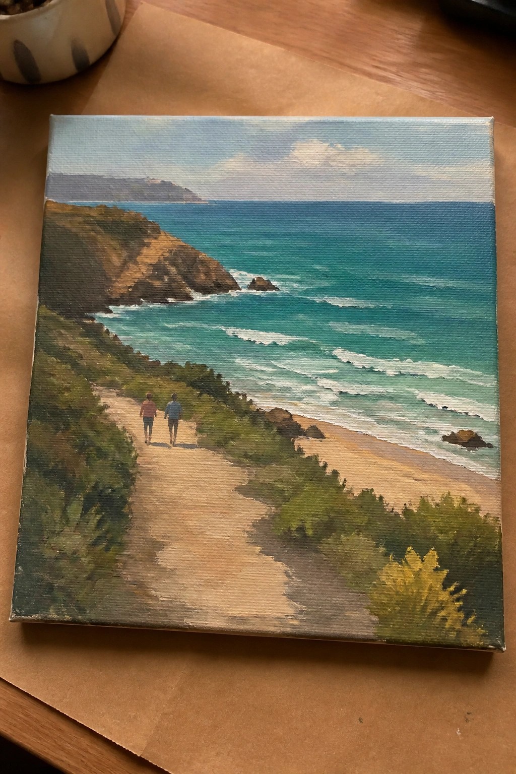 Landscape painting of two hikers on cliff path above turquoise ocean waves and beach.