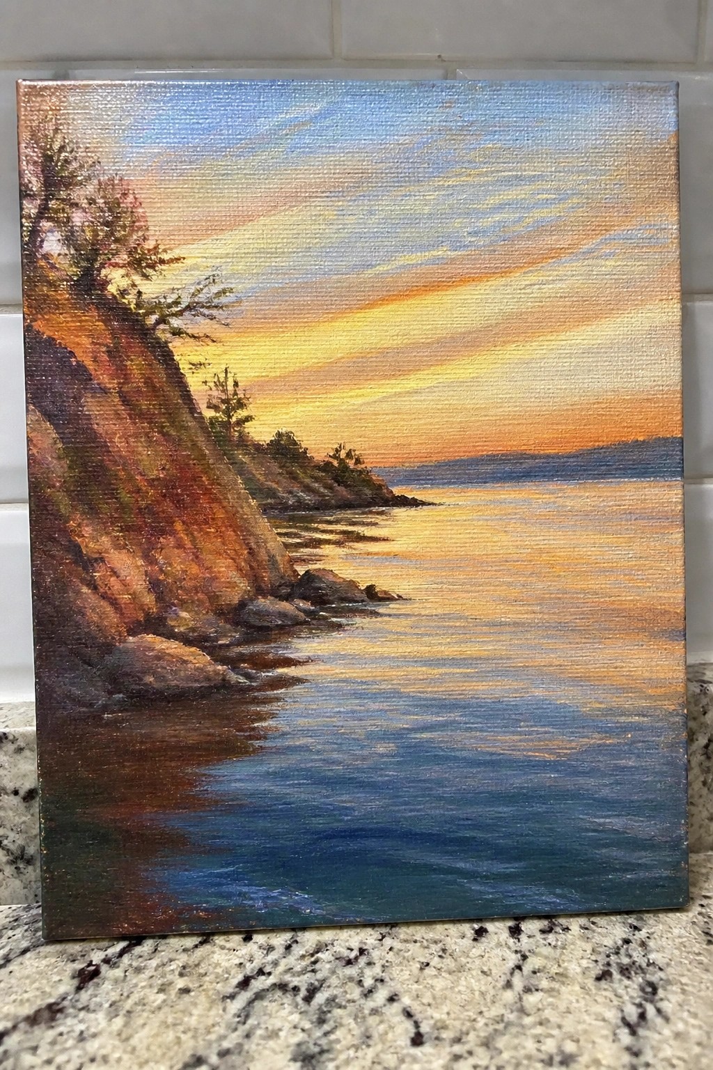 Vibrant sunset painting with orange skies reflecting on calm waters beside rocky cliffs
