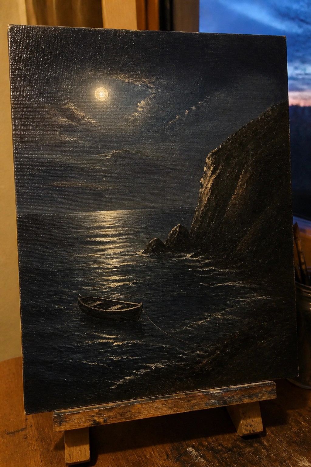 Moonlit ocean painting with small boat, rocky cliffs, and glowing full moon on easel