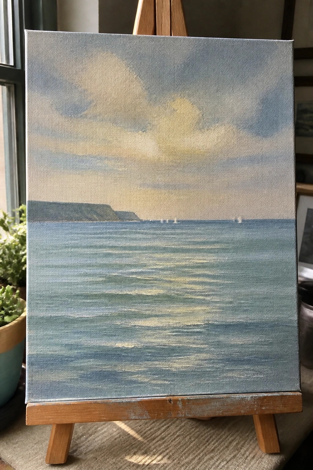 Seascape painting on wooden easel showing blue waves, cliffs, and distant sailboats