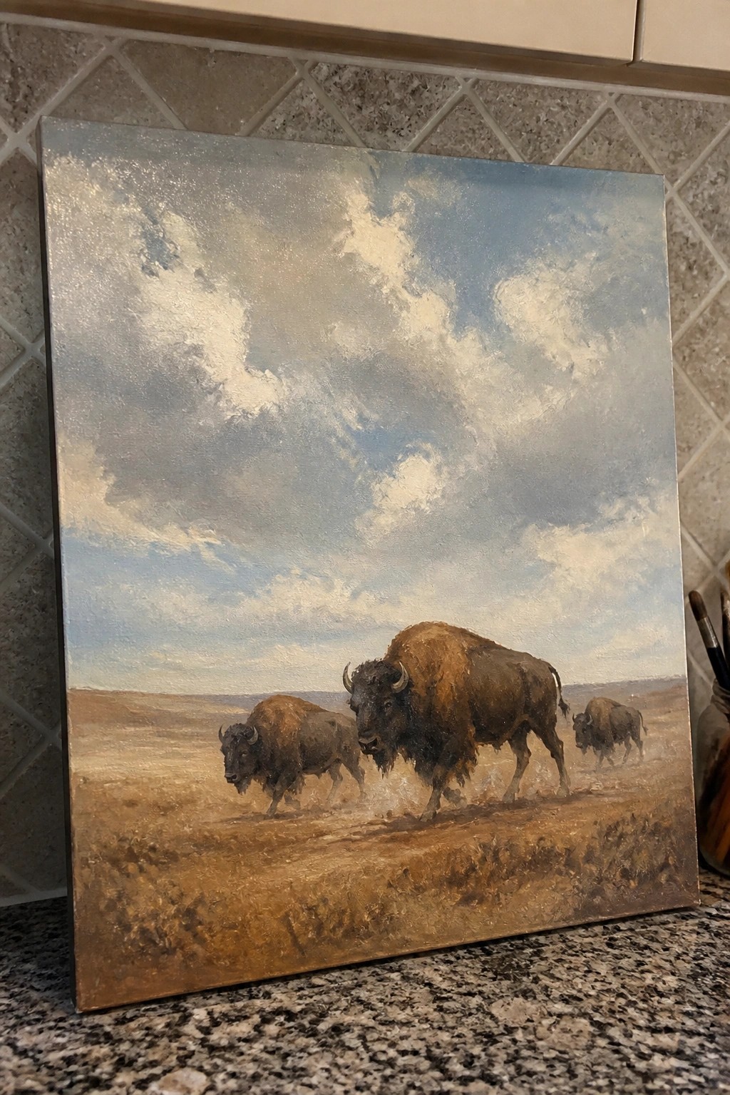 Three bison walking across a dusty prairie under a vast cloudy sky