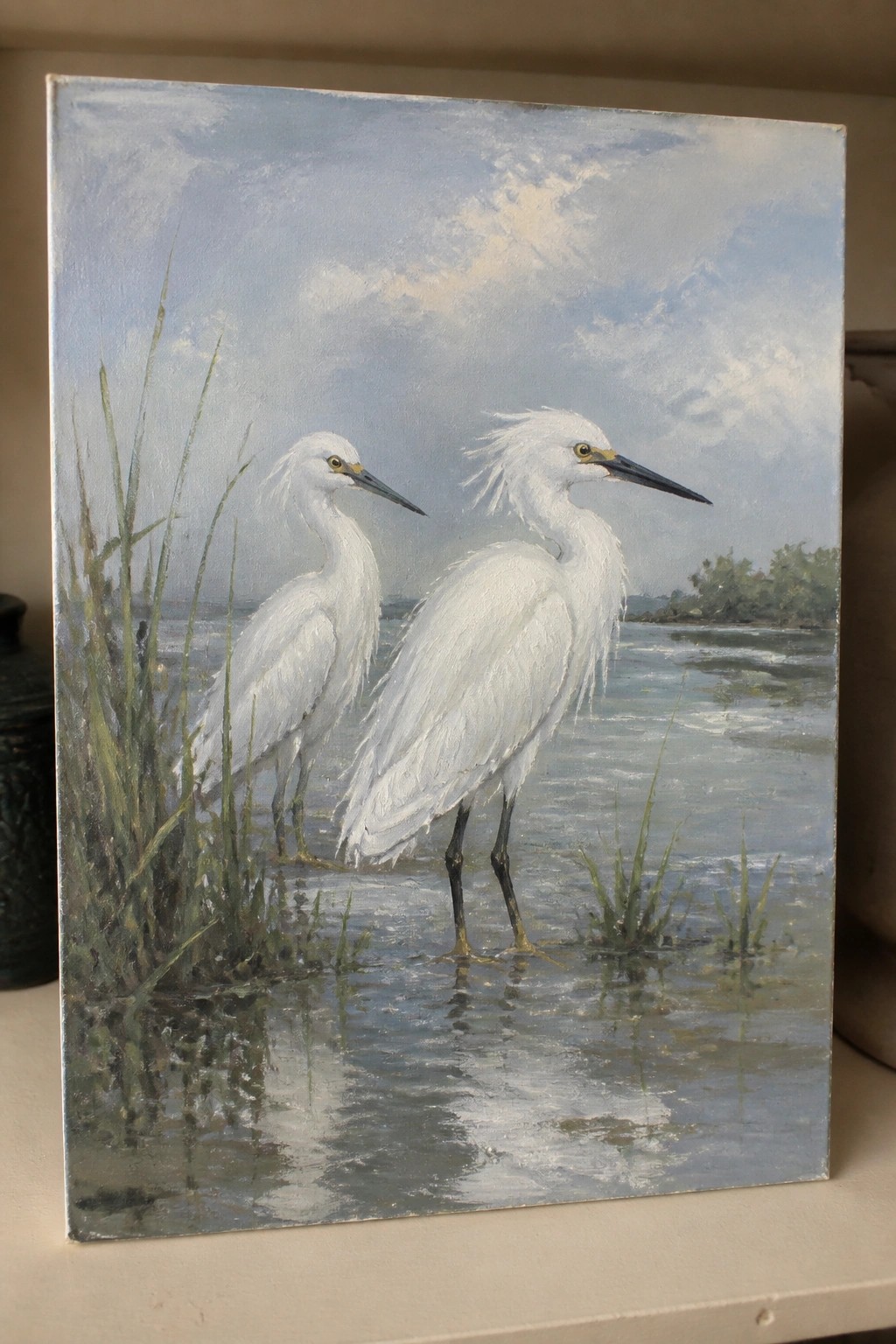 Two white egrets wade in shallow reflective water amid green reeds under clouds