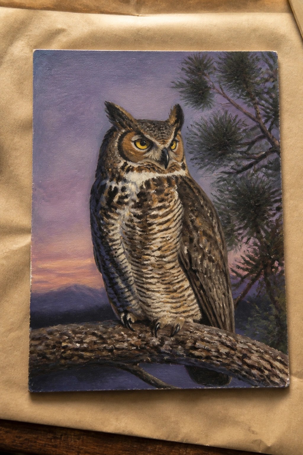 Realistic painting of great horned owl perched on branch against purple-orange dusk sky with pines