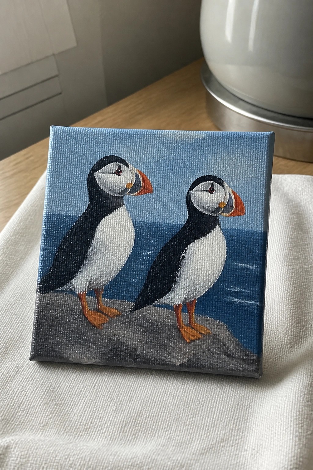 Small canvas painting of two puffins on a rock by blue sea