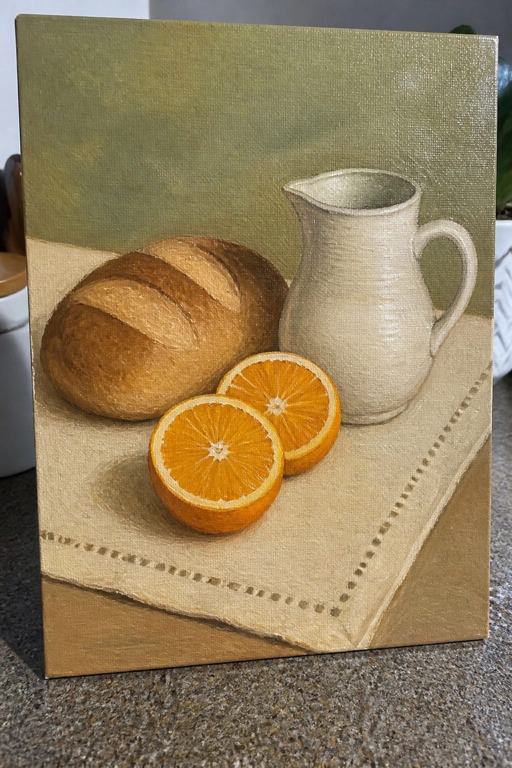 Still life with brown bread loaf, orange slices, white pitcher on beige cloth.