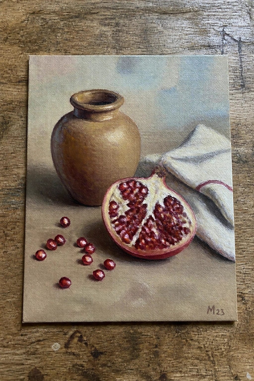 Still life with brown vase, halved pomegranate, scattered seeds, and white cloth.