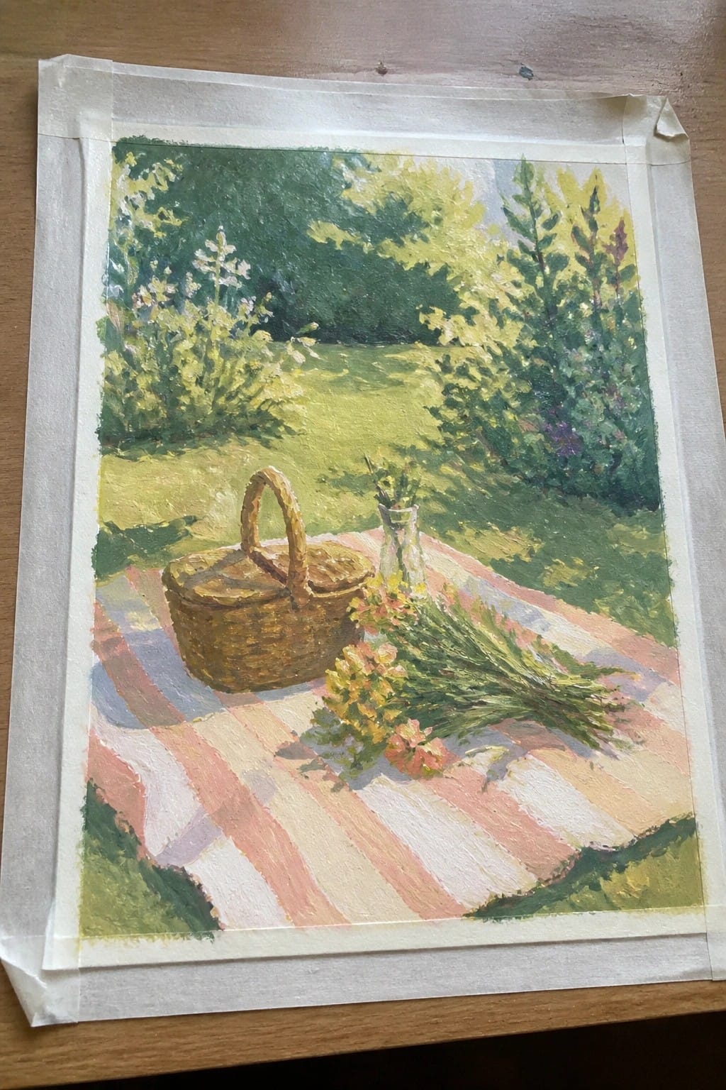 Wicker picnic basket and flowers on red-striped blanket in sunny grassy meadow with trees