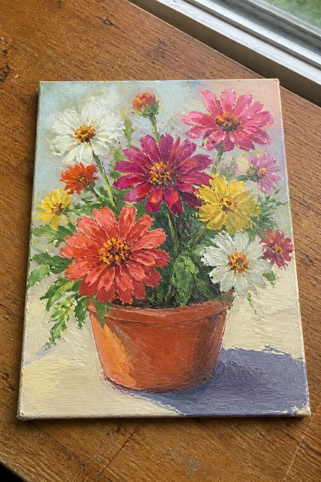 Vibrant painting of colorful flowers blooming in a terracotta pot on wood.