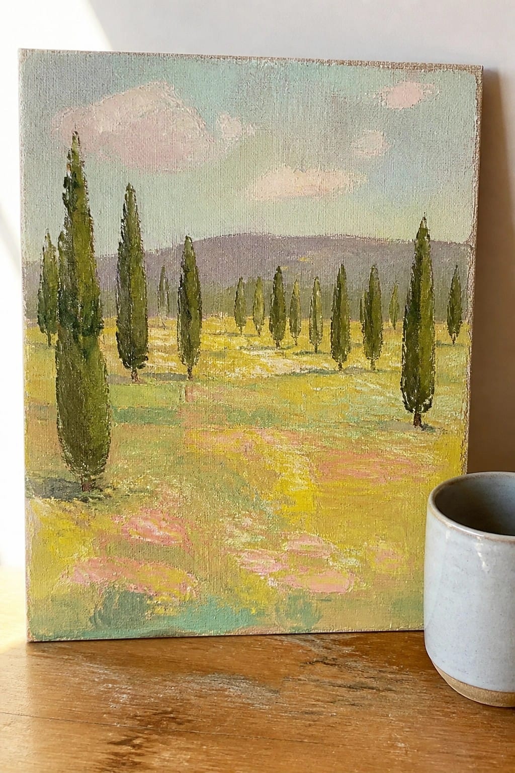 Canvas painting of cypress trees in a yellow field beside a blue mug