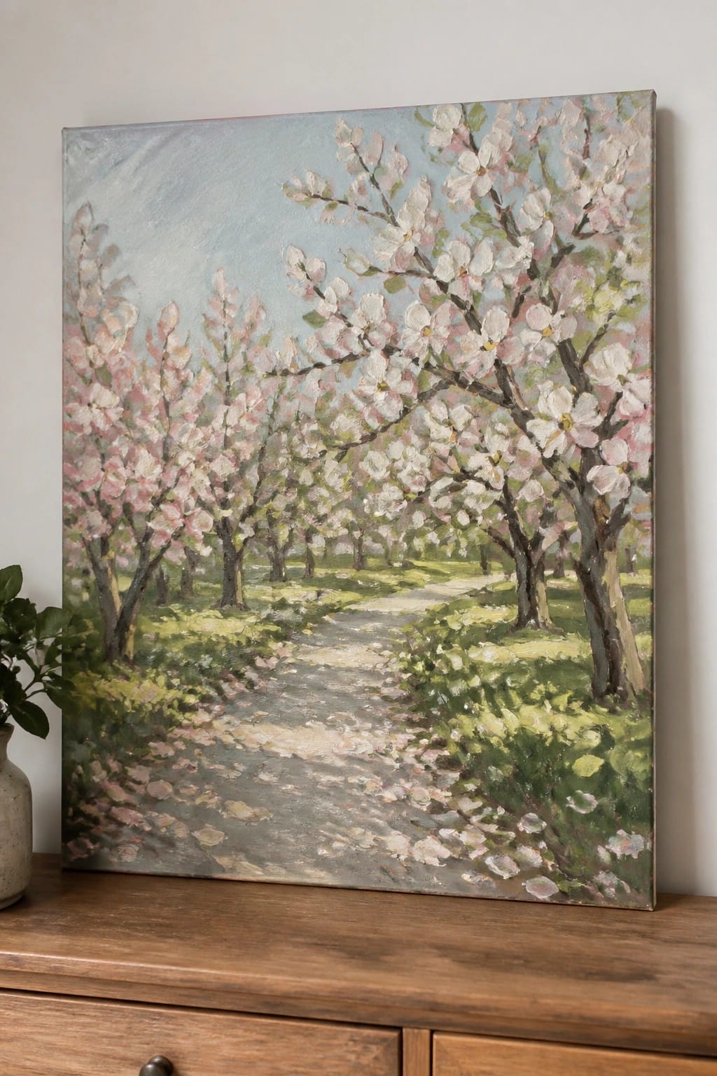 Oil painting of a winding path through blooming pink and white trees on a wooden dresser.