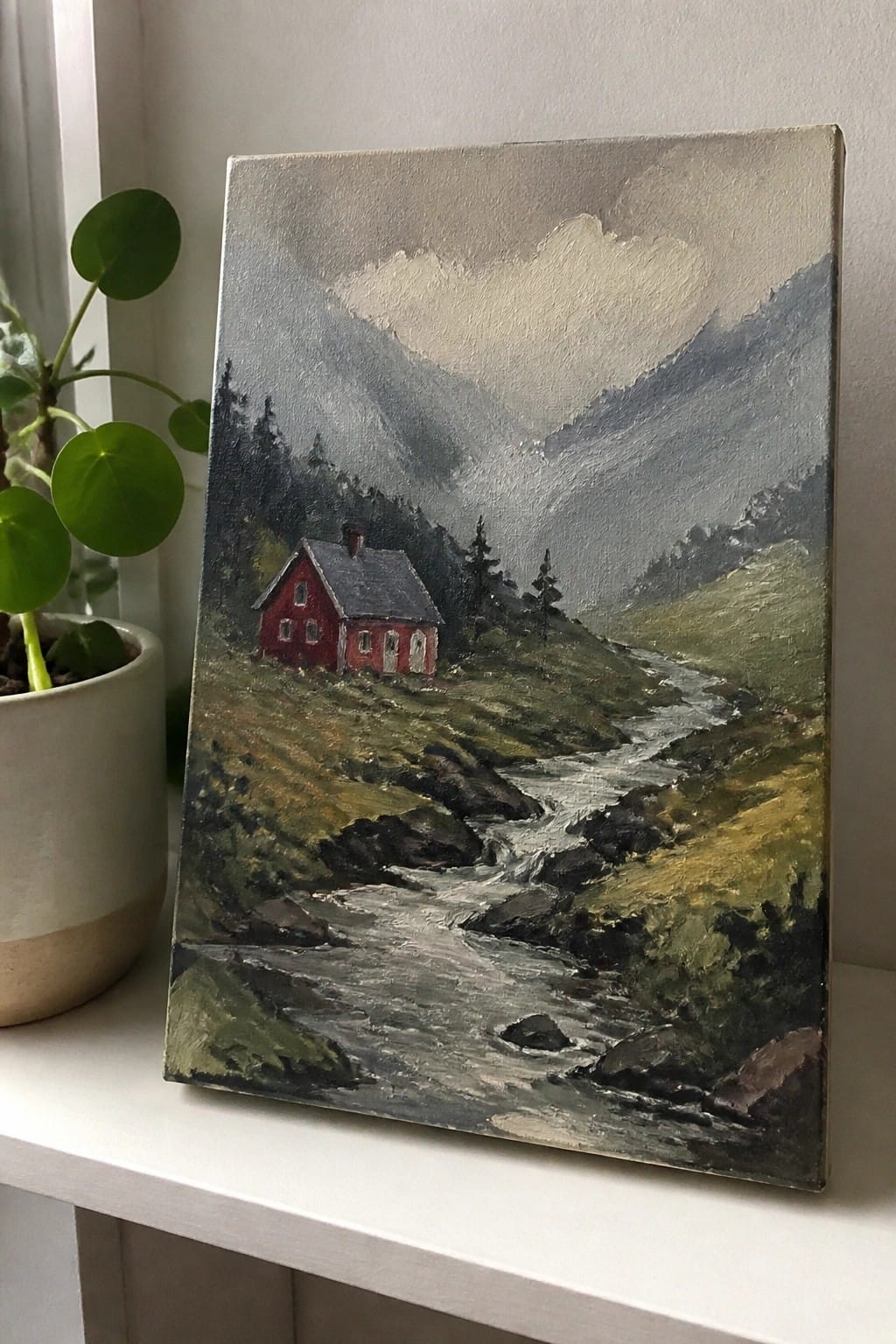 Red cabin painting by rocky stream in misty mountains beside potted plant