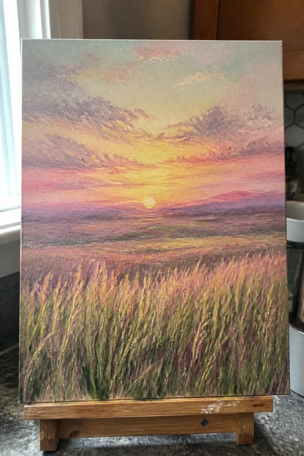 Vibrant sunset painting with pink-orange sky over tall grass field on wooden easel
