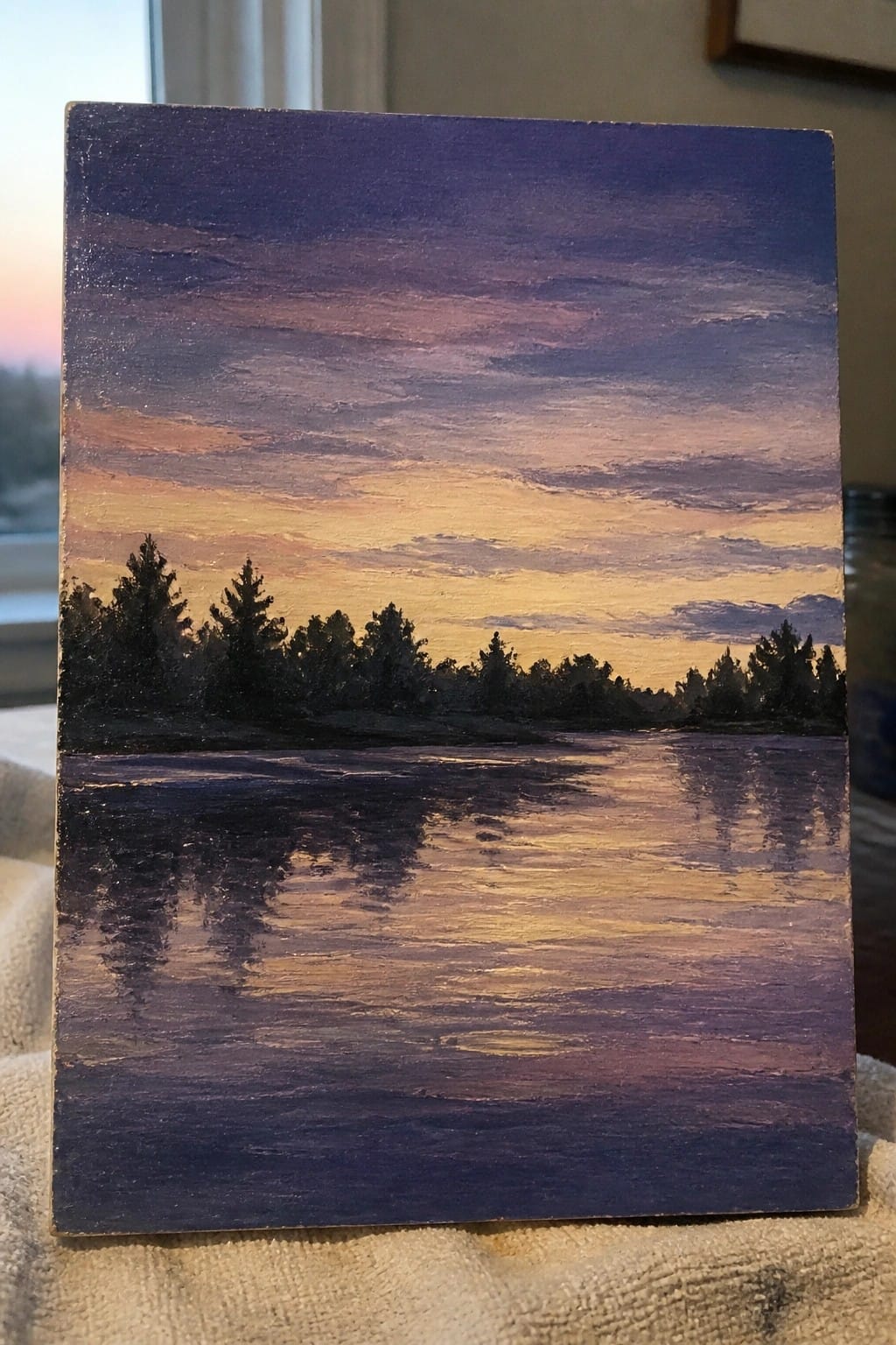 Painting of sunset with purple-orange sky, silhouetted trees, and reflections on calm water.