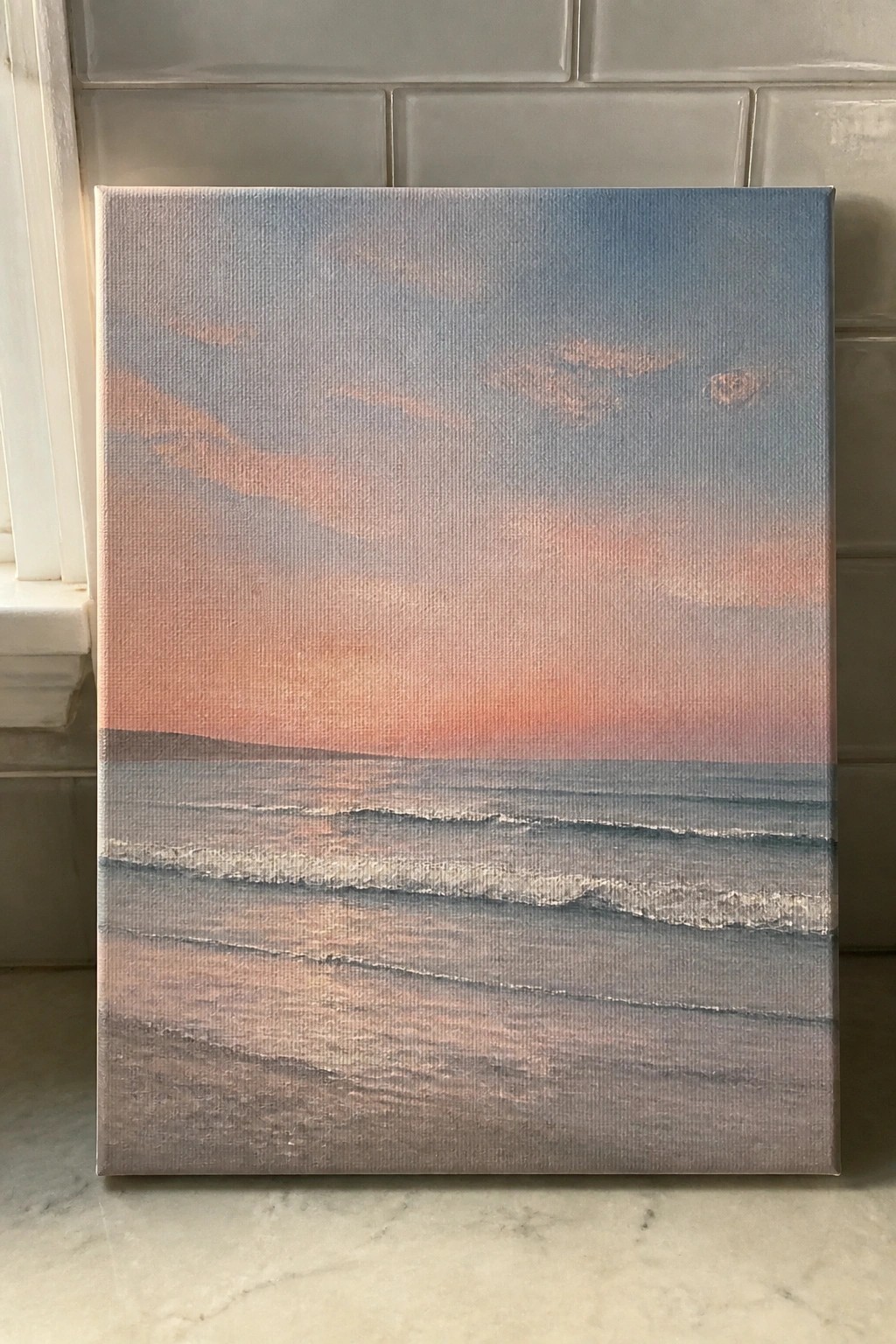 Painting of pink sunset over gray ocean waves on canvas leaning by tiles