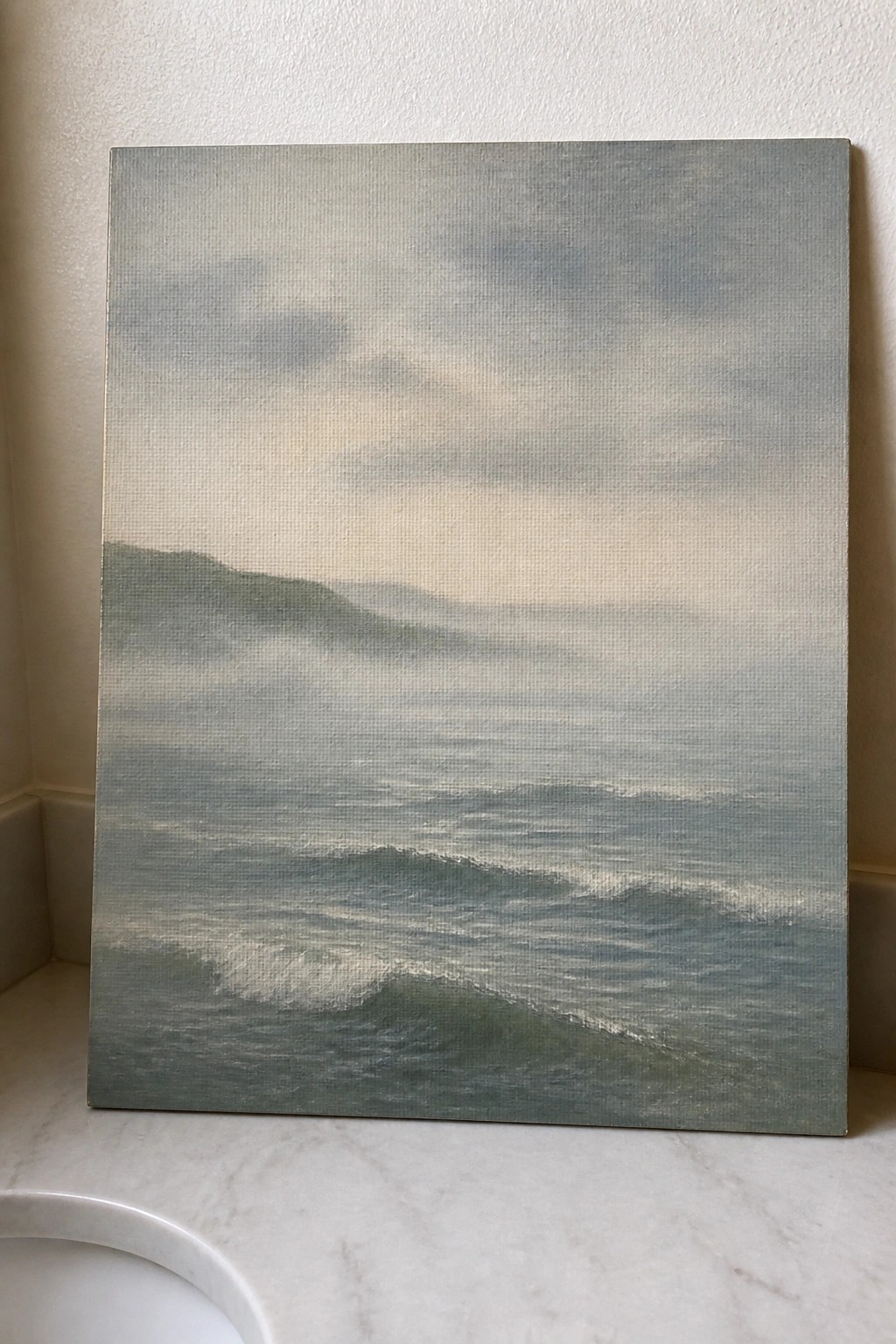 Misty seascape painting with rolling waves and distant hills on marble ledge