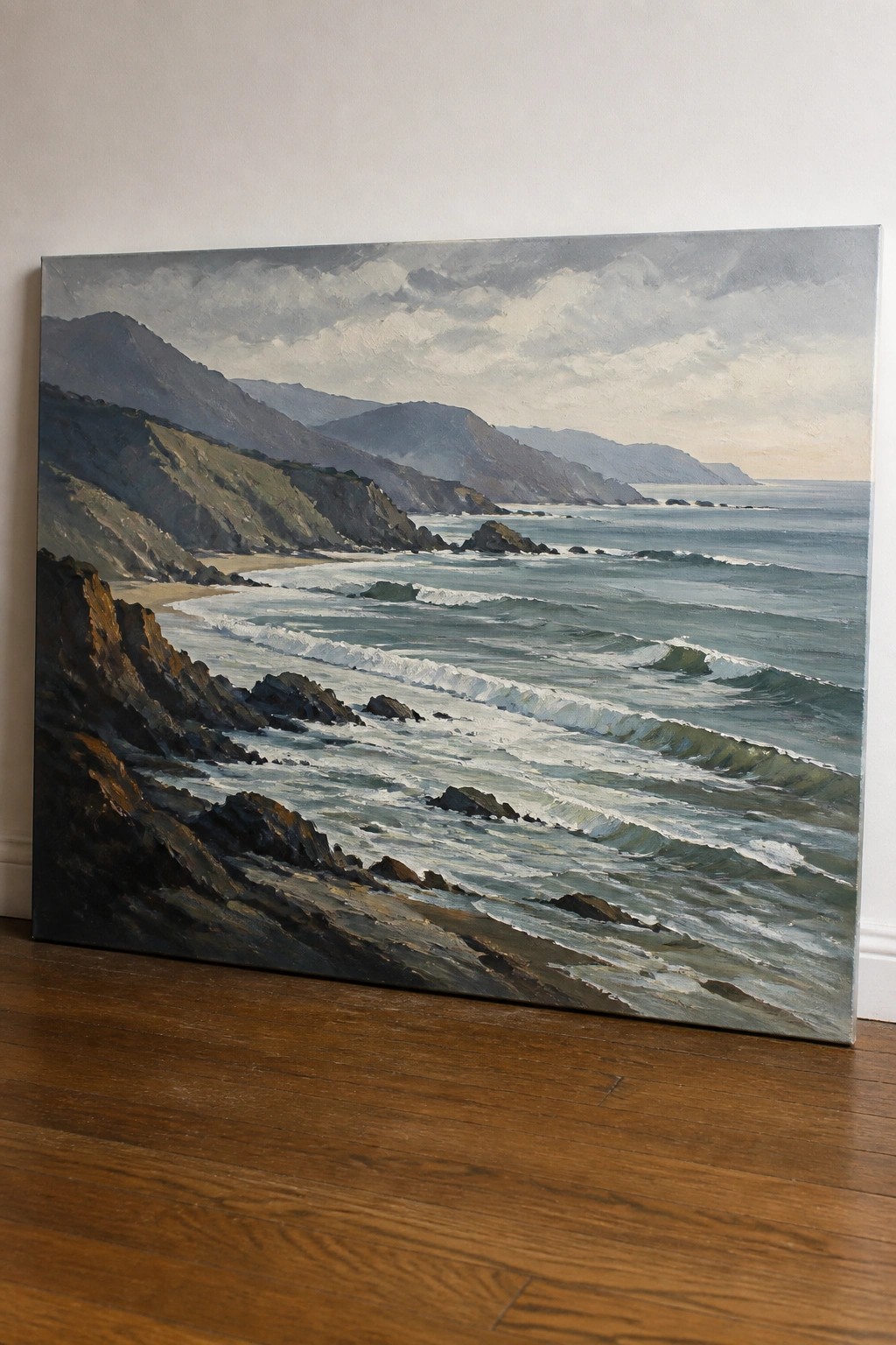 Large oil painting of waves crashing on rocky coast with mountains under cloudy sky