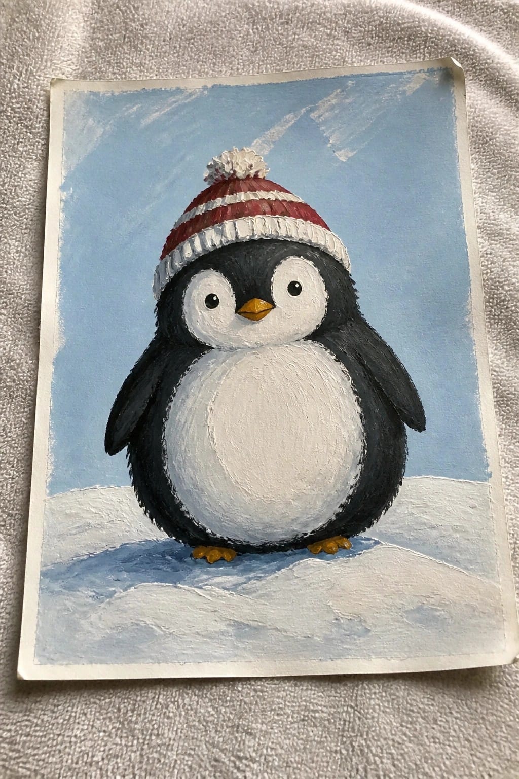 Penguin in red-and-white striped knit hat with pom-pom on snowy ground under blue sky.